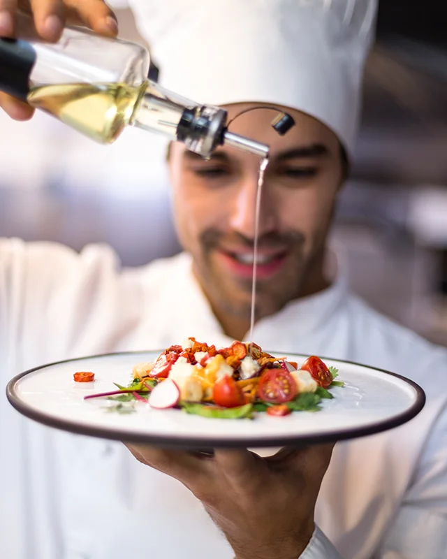 A chef pouring oil onto a plate of food